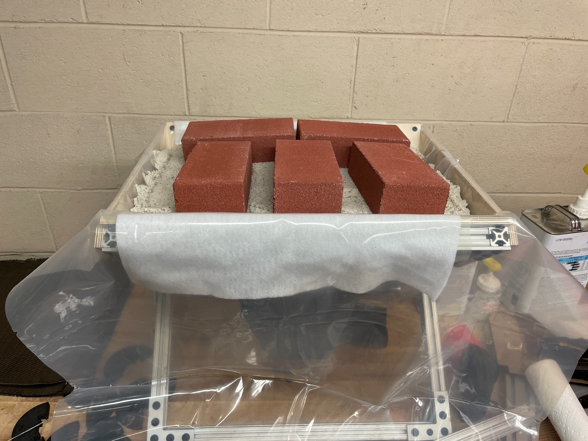 Sand and bricks loading a flexible membrane over a composite layup fixture